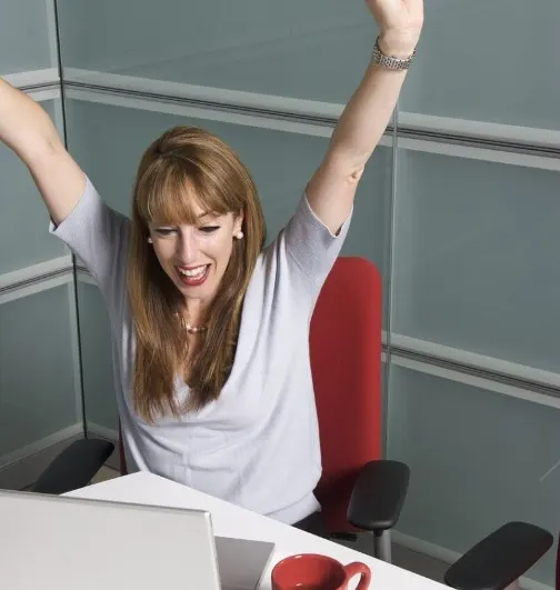 An adult throwing her arms up in celebration after understanding something at her laptop