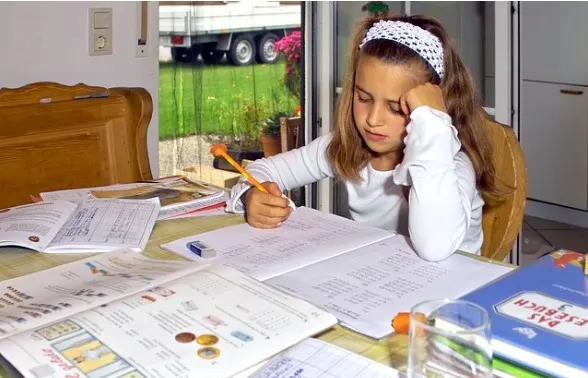 A child resting her head on her hand, tired and stuck on a homework worksheet