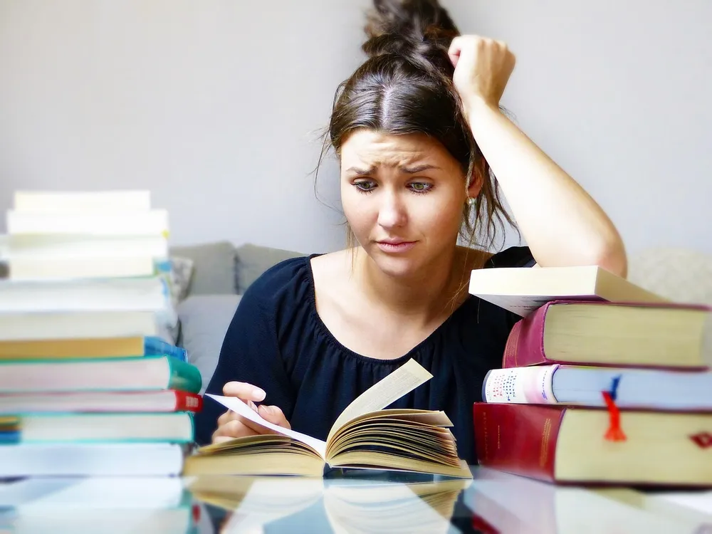 A worried student with her hand on her head, looking at an open book