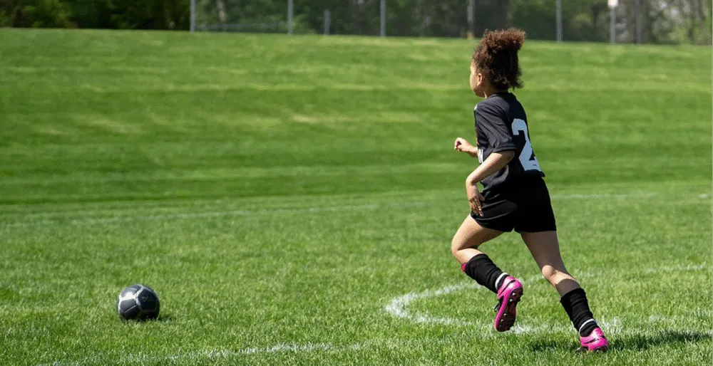 A girl kicking a football on a green field