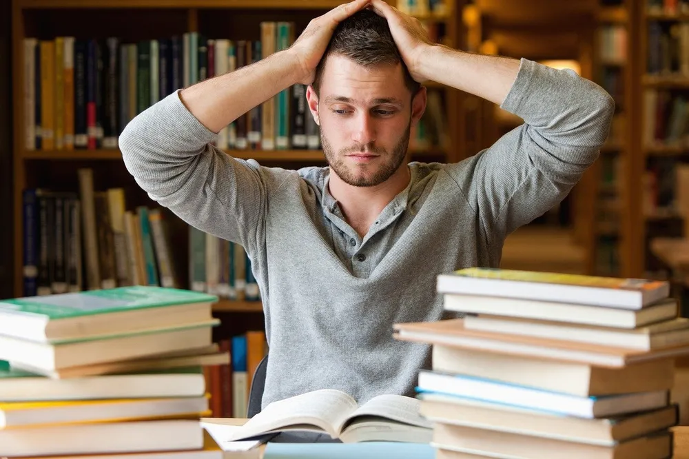 A stressed student holding his head among piles of books