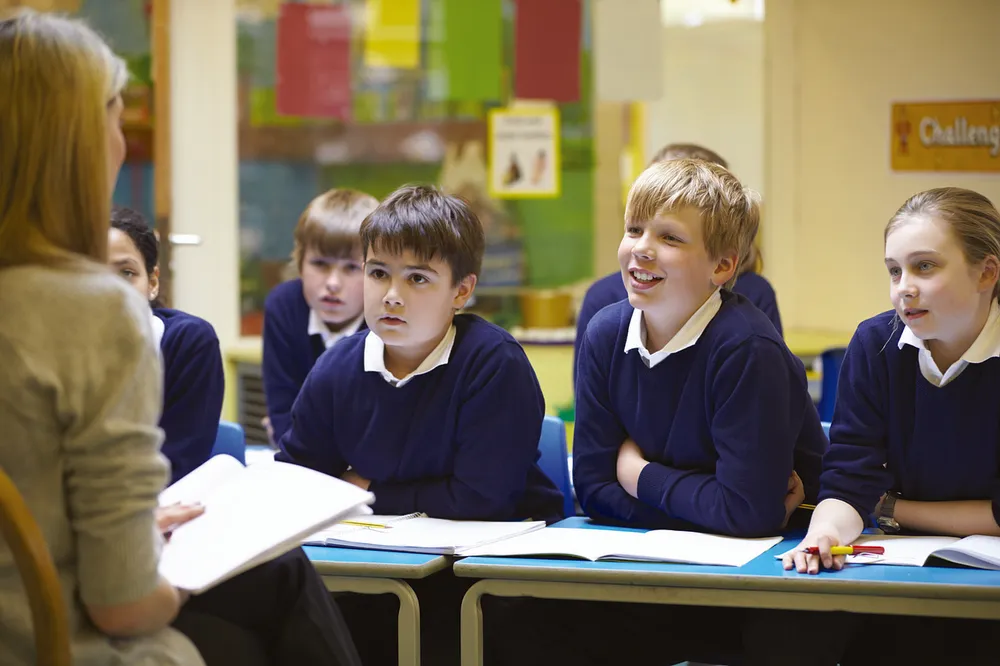 Pupils in uniform working at their desks while the teacher watches